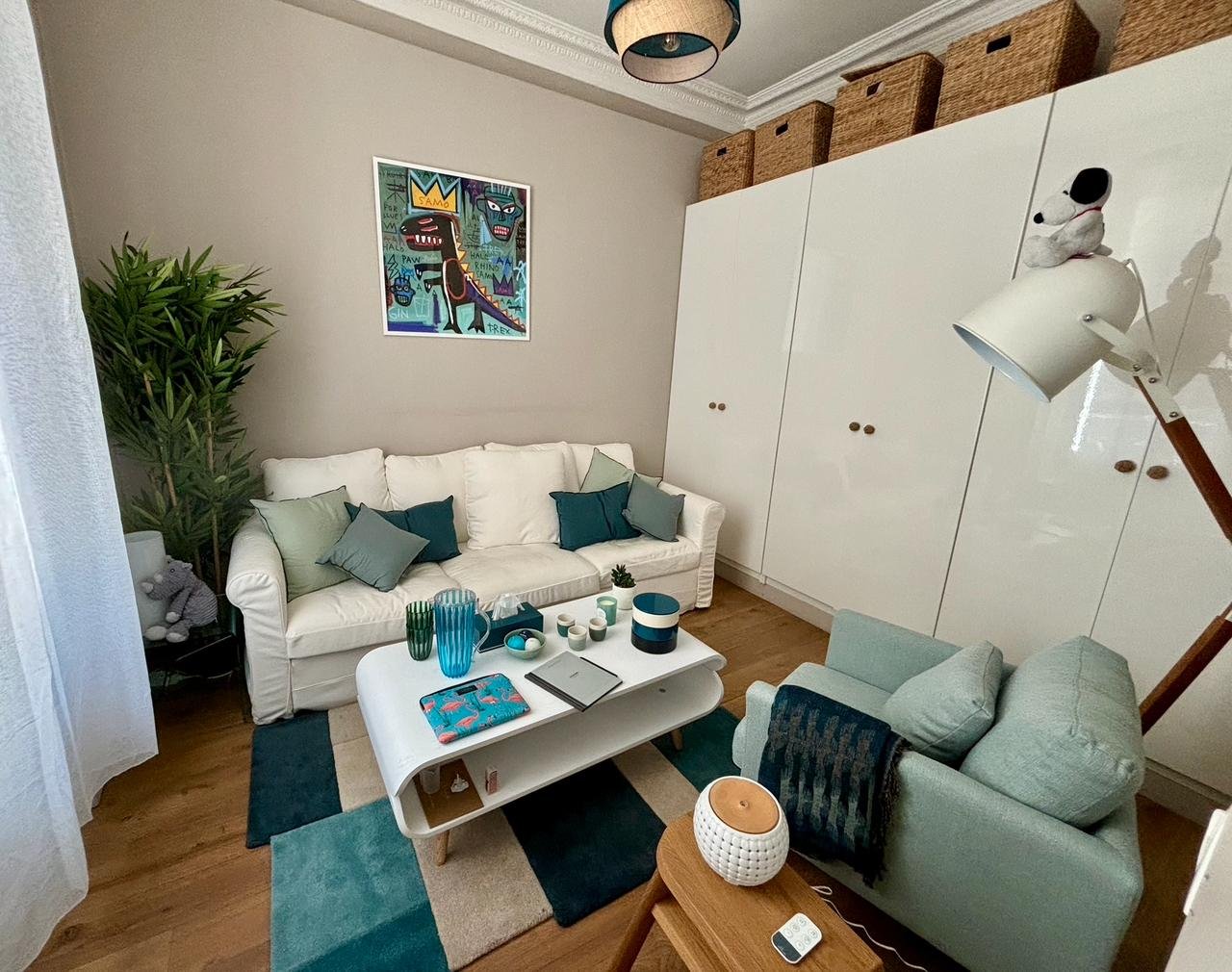 Vue large du cabinet — deux canapés (blanc et vert sauge), table basse, lampe Snoopy, ambiance lumineuse